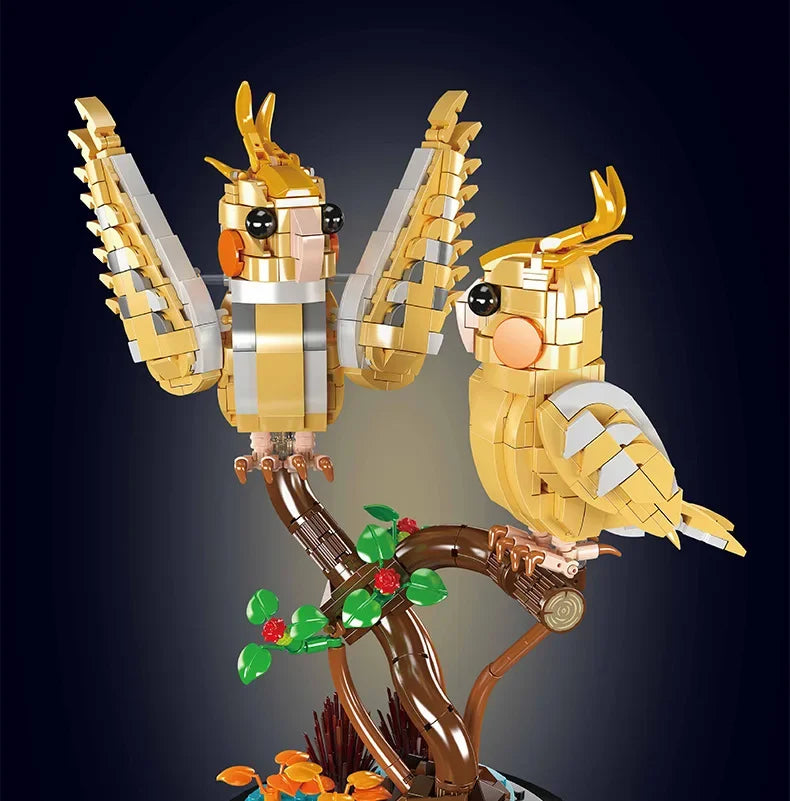 Two golden brick birds on a brown branch with green and red flower accents