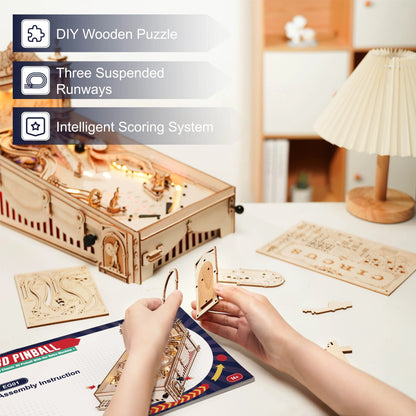 Wooden pinball machine assembly with hands placing wooden parts and lit playfield